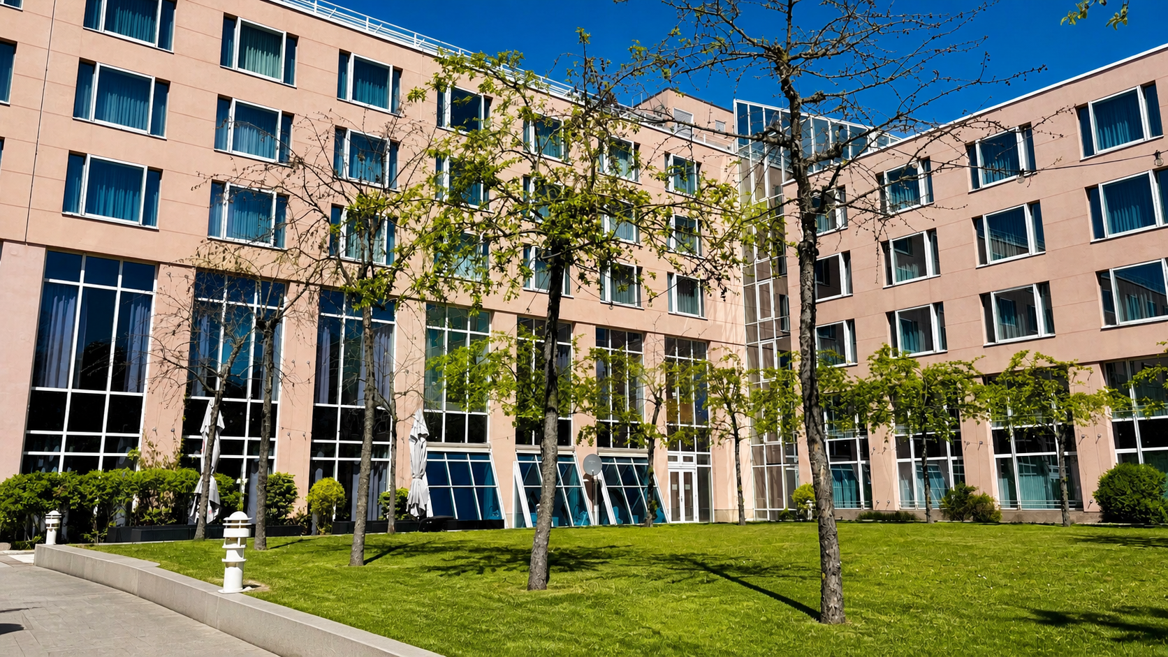 Hotelgebäude mit großen Fenstern, einer Rasenfläche und jungen Bäumen davor.