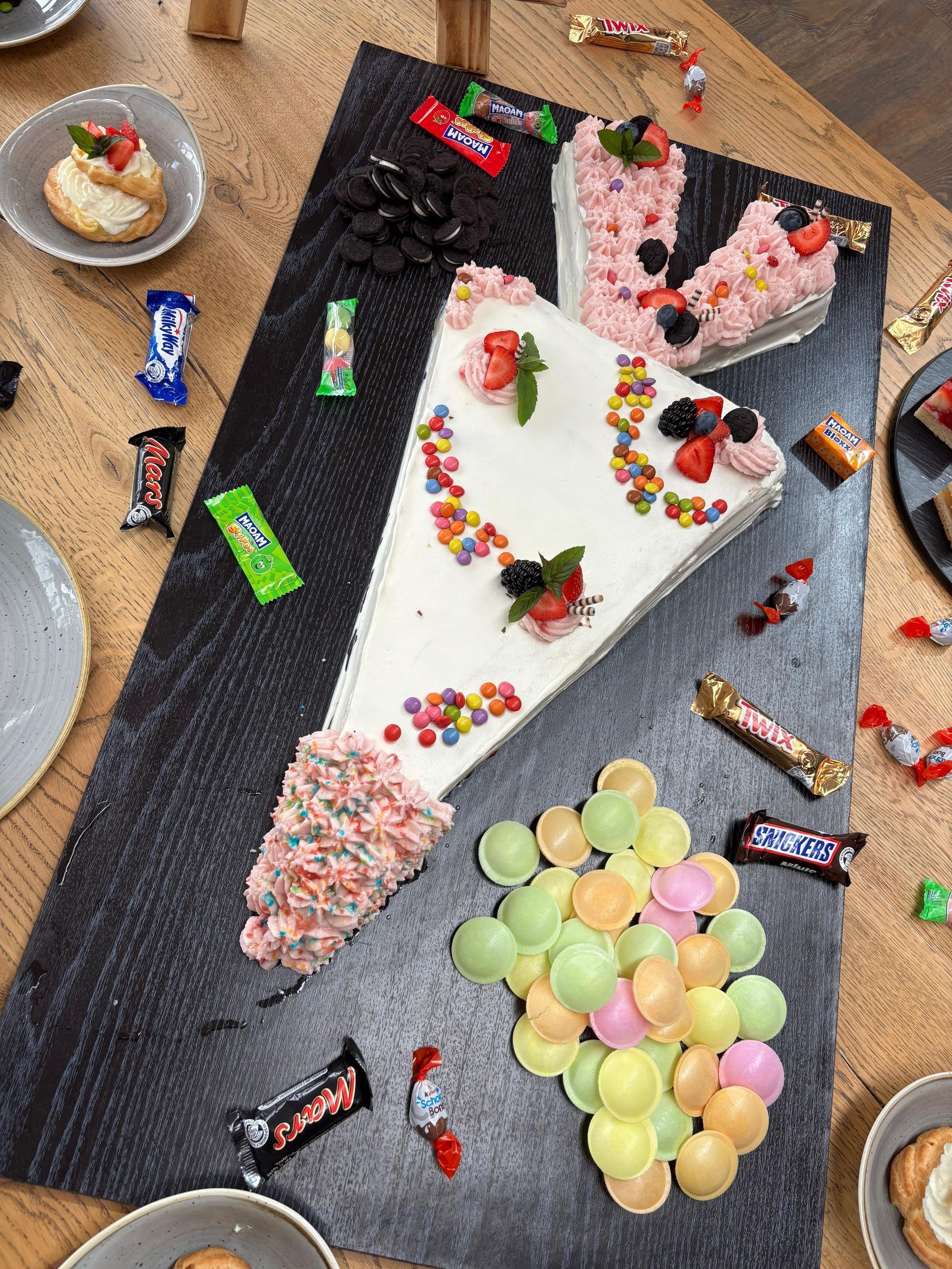 Ein mit Süßigkeiten und Früchten dekoriertes Kuchenstück auf einer Platte, umgeben von Süßigkeiten und anderen Desserts.