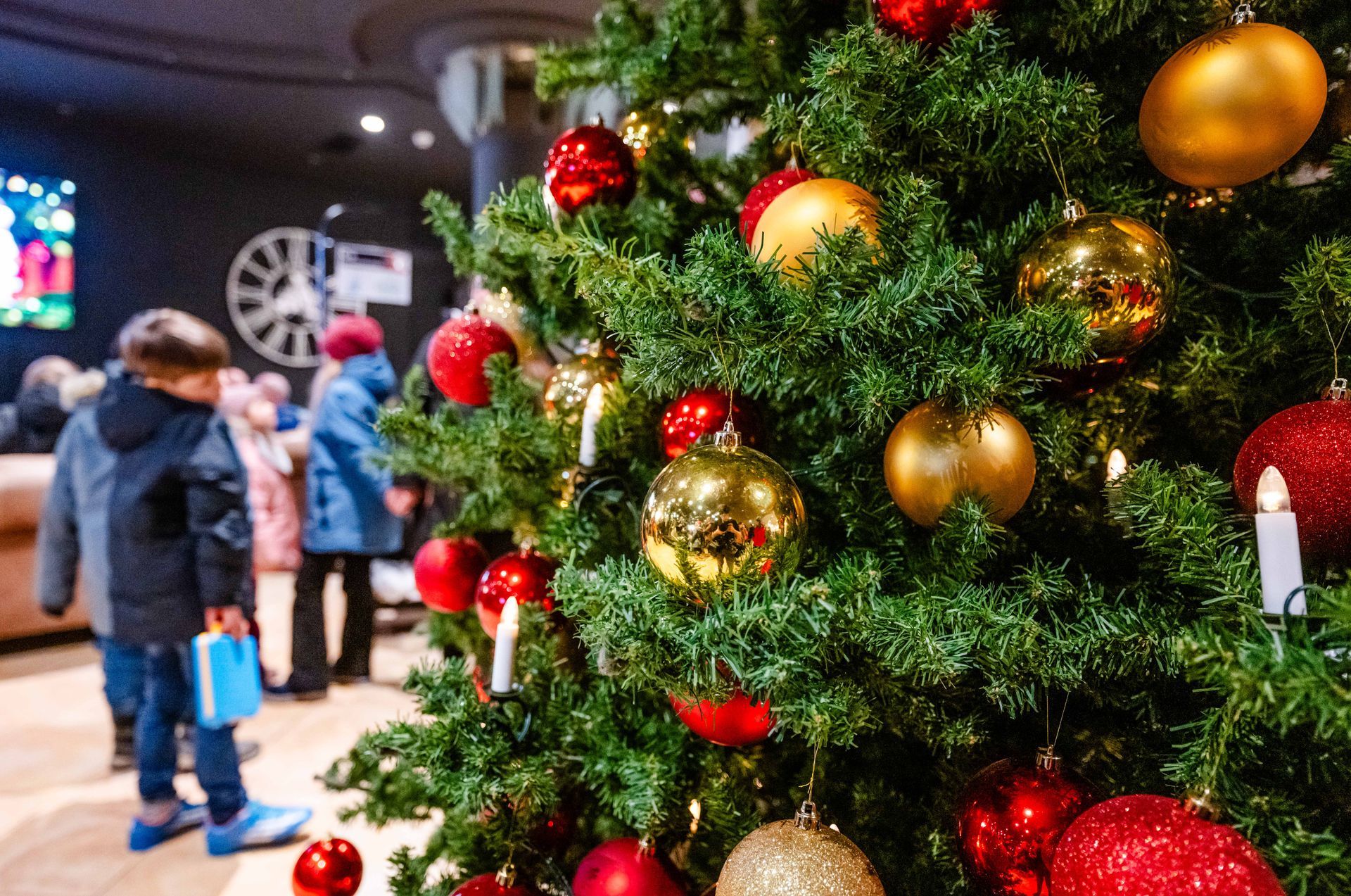 Weihnachtsbaum mit rotem und goldenem Schmuck, Menschen im Hintergrund.