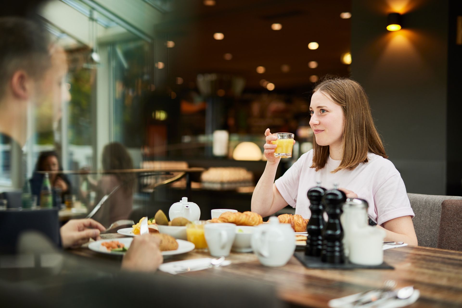 Zwei Personen sitzen an einem Tisch im Restaurant; eine hält ein Glas Orangensaft.
