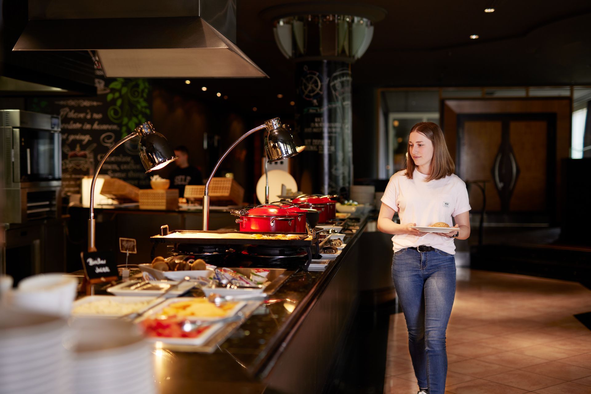 Eine Person geht an einem Restaurantbuffet mit warmer Beleuchtung vorbei und hält einen Teller in den Händen.