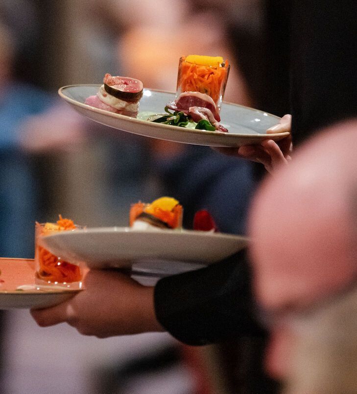 Kellner tragen Teller mit Vorspeisen und Getränken bei einer Catering-Veranstaltung.