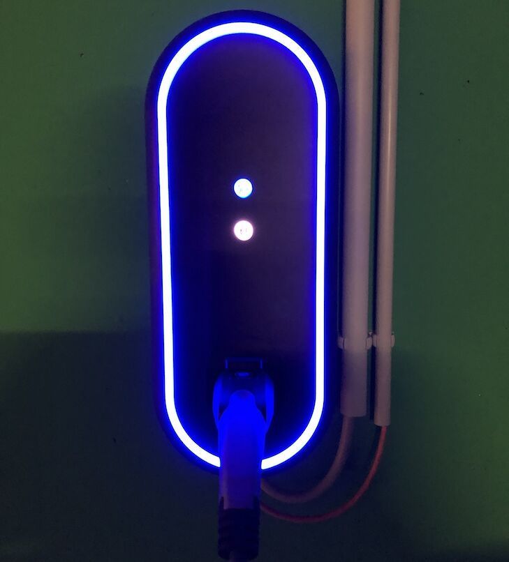 Ladestation für Elektrofahrzeuge an grüner Wand, blau beleuchtet, mit angeschlossenem Ladekabel.