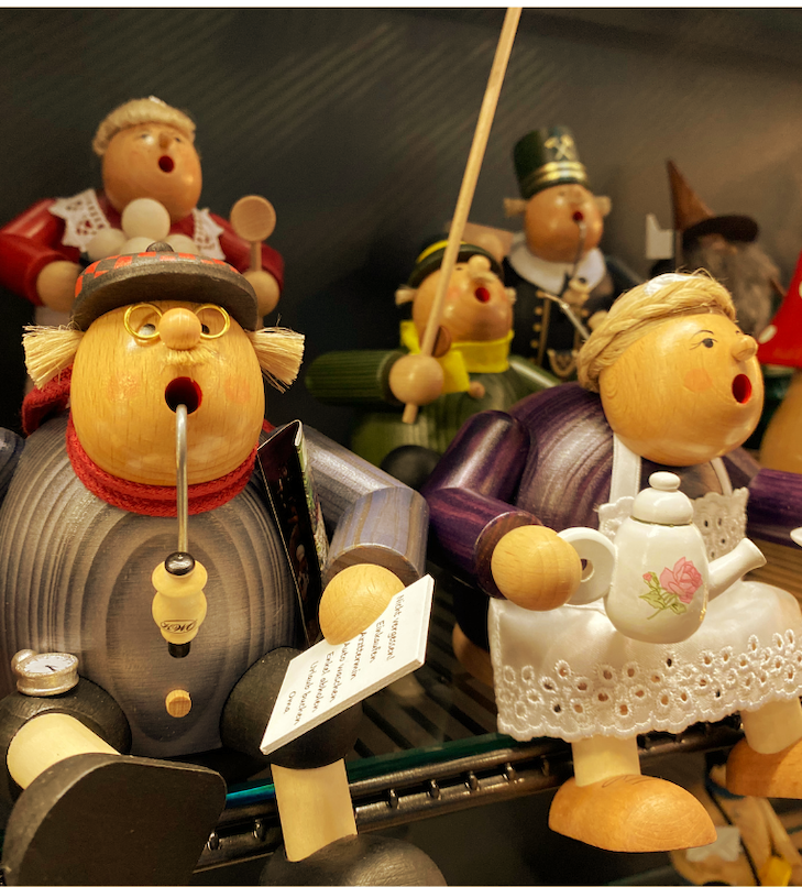 Auf einem Regal ausgestellt sind singende Holzfiguren, die Gegenstände wie Pfeifen und Teekannen halten, einige mit Hüten.
