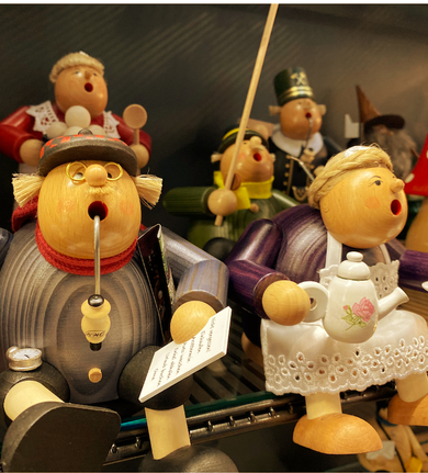 Auf einem Regal ausgestellt sind singende Holzfiguren, die Gegenstände wie Pfeifen und Teekannen halten, einige mit Hüten.
