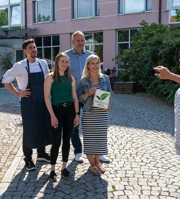 Eine Gruppe von vier Personen steht draußen und hält ein Schild mit der Aufschrift „Green Sign“.
