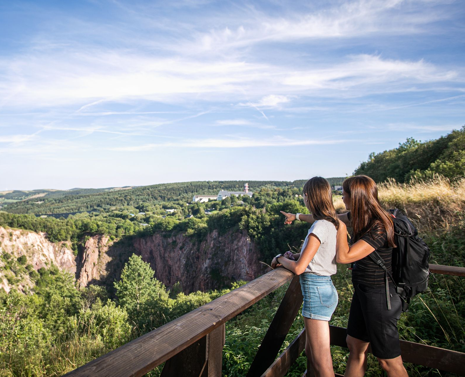 Zwei Personen blicken an einem sonnigen Tag von einem Holzgeländer aus in eine Schlucht.