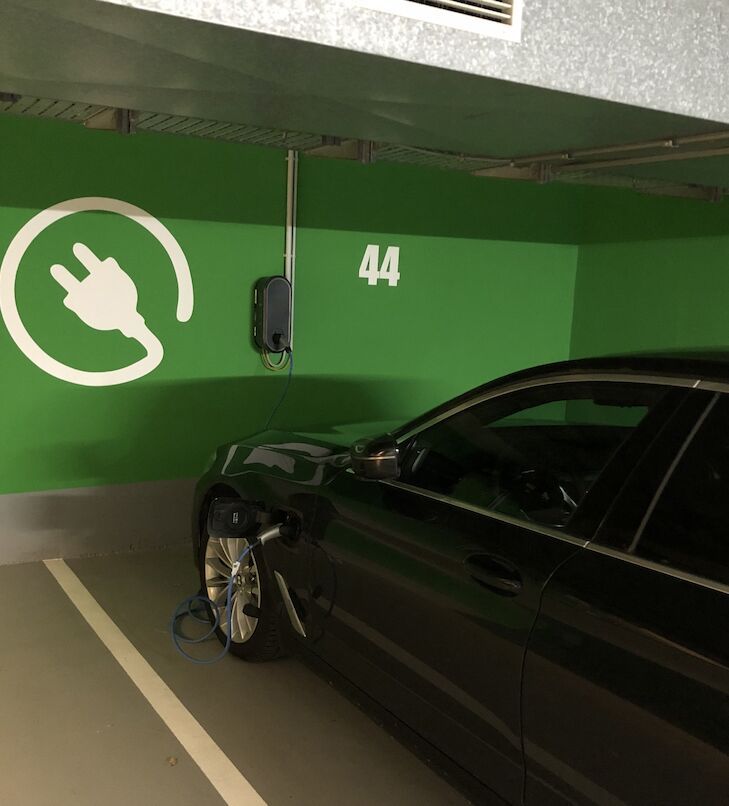 Ladestation für Elektrofahrzeuge in einem Parkhaus. Grüne Wand mit den Nummern 42 und 43. Weißes Ladesymbol.