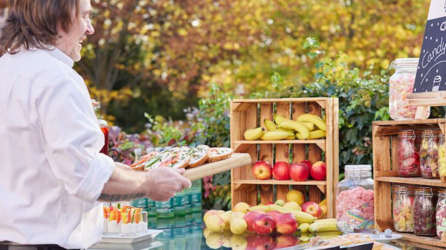 Ein Mitarbeiter des c/o56 Chemnitz arrangiert Obst auf einem Markttisch im Freien – Äpfel, Birnen und Gläser.