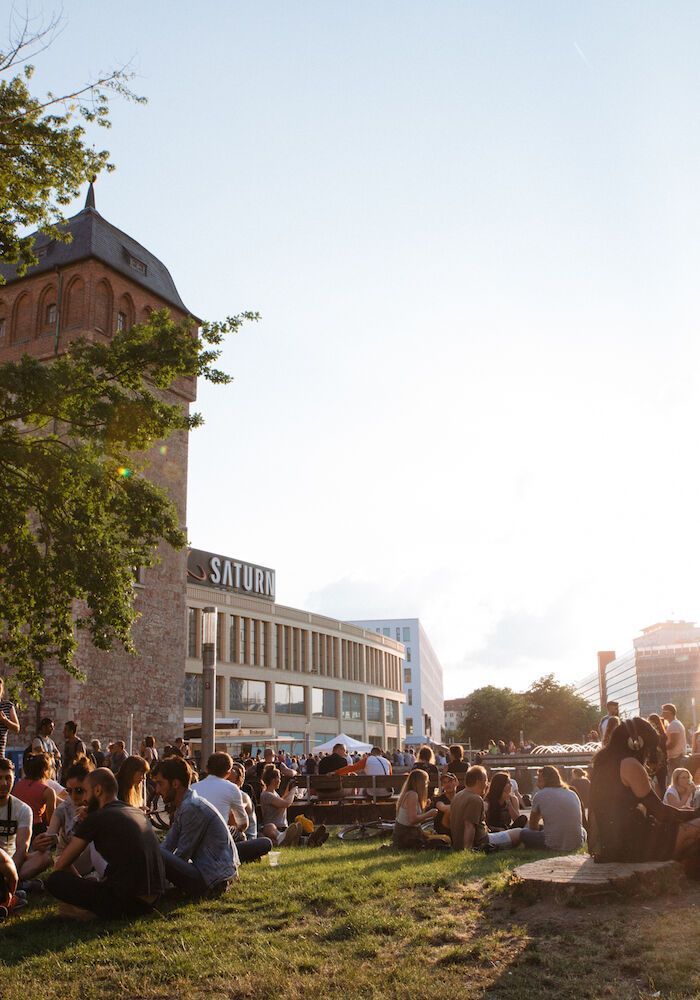 Menschen versammeln sich auf Rasenflächen in der Nähe von Gebäuden; sonniger Tag.