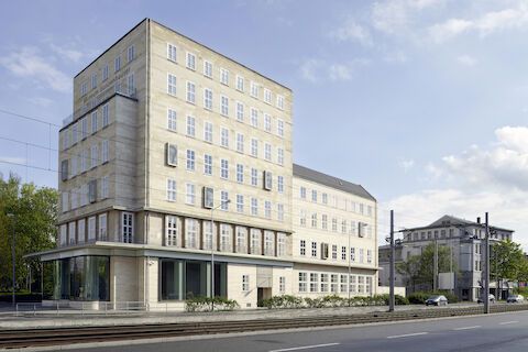 Modernes Bürogebäude aus Beton mit mehreren Stockwerken und Flachdach, in der Nähe einer Straße.