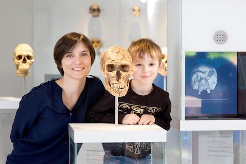 Frau und Kind posieren mit einem Totenkopf-Exponat in einem Museum.