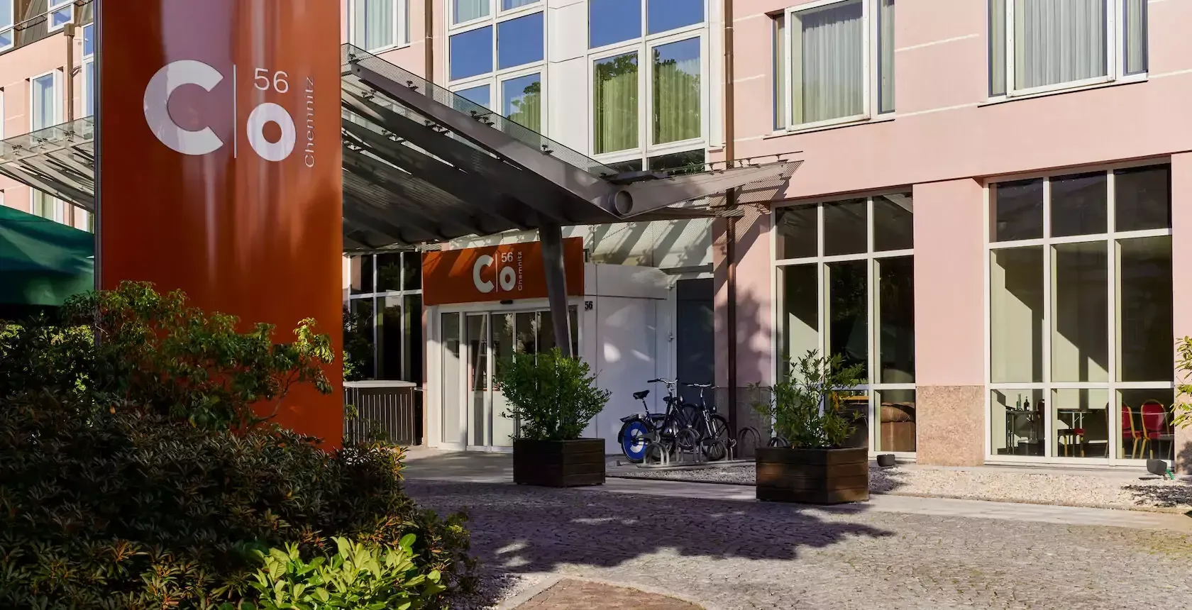 Hoteleingang mit orange-weißem Schild „C&o“ und rosafarbener Gebäudefassade.