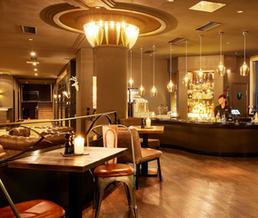 Gemütliches Bar-Interieur mit warmer Beleuchtung, Holzböden und einem Barkeeper hinter der Theke.