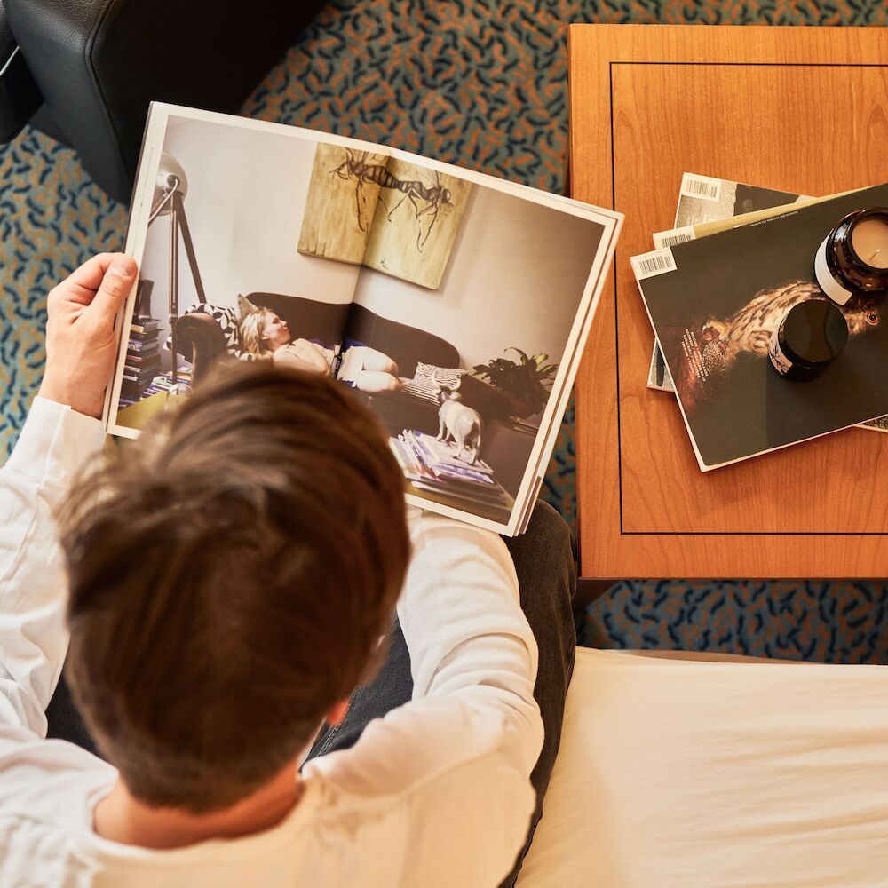 Eine Person betrachtet ausgedruckte Fotos auf einem Tisch; ein großes Foto ist aufgeschlagen, ein weiteres liegt daneben.