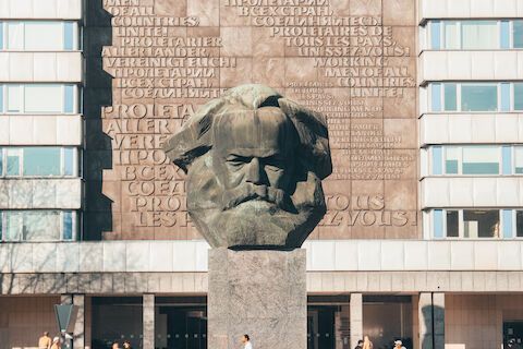 Monumentale Büste von Karl Marx in Berlin, Deutschland. Graue Skulptur auf einem Steinsockel, im Hintergrund eine Fassade.