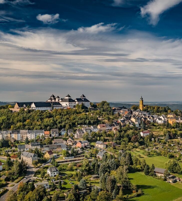 Blick auf eine auf einem Hügel gelegene Stadt mit Burg, Kirche und Häusern unter bewölktem Himmel.