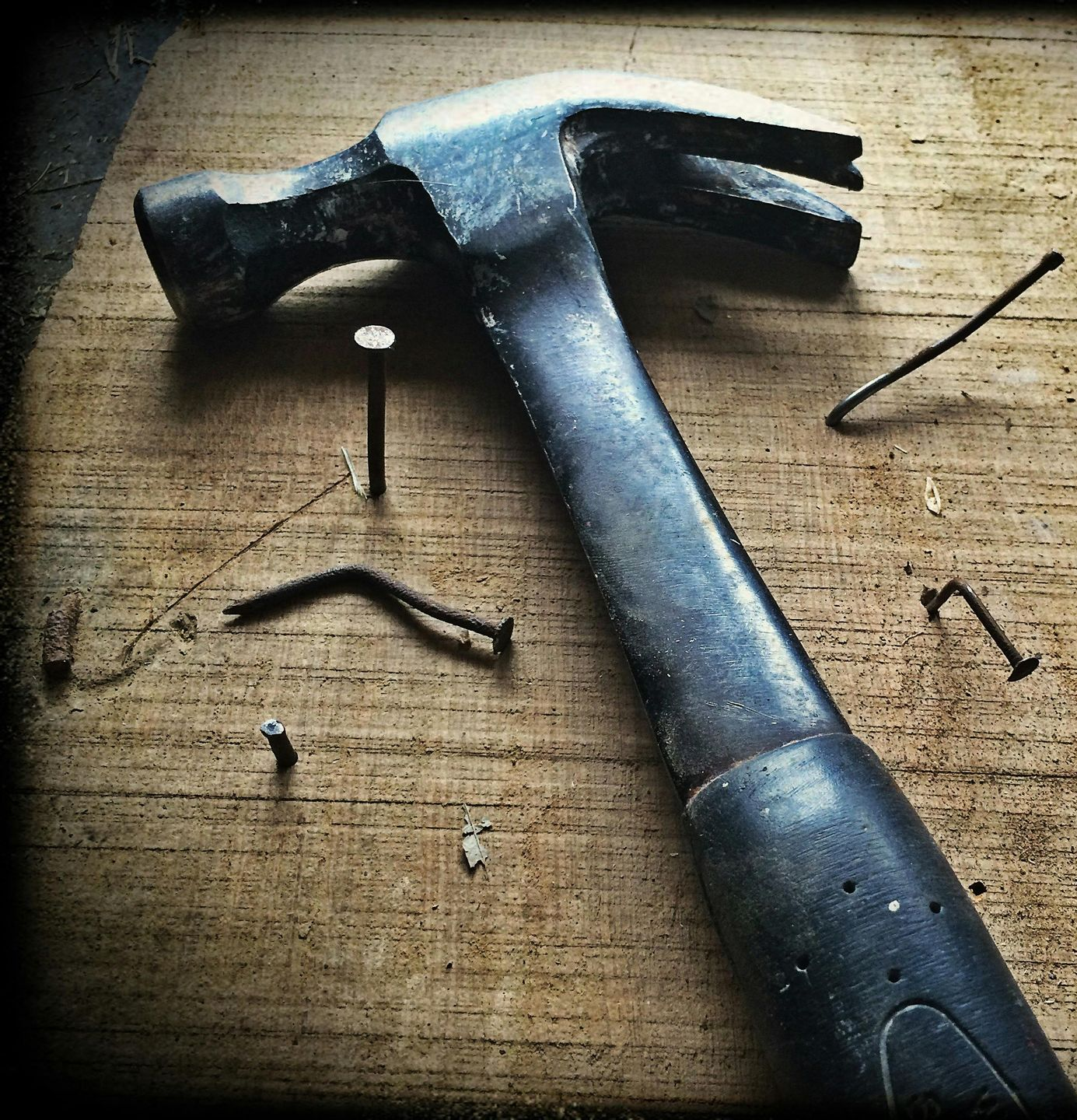 Ein Hammer liegt auf einem Holzbrett mit verstreuten Nägeln.