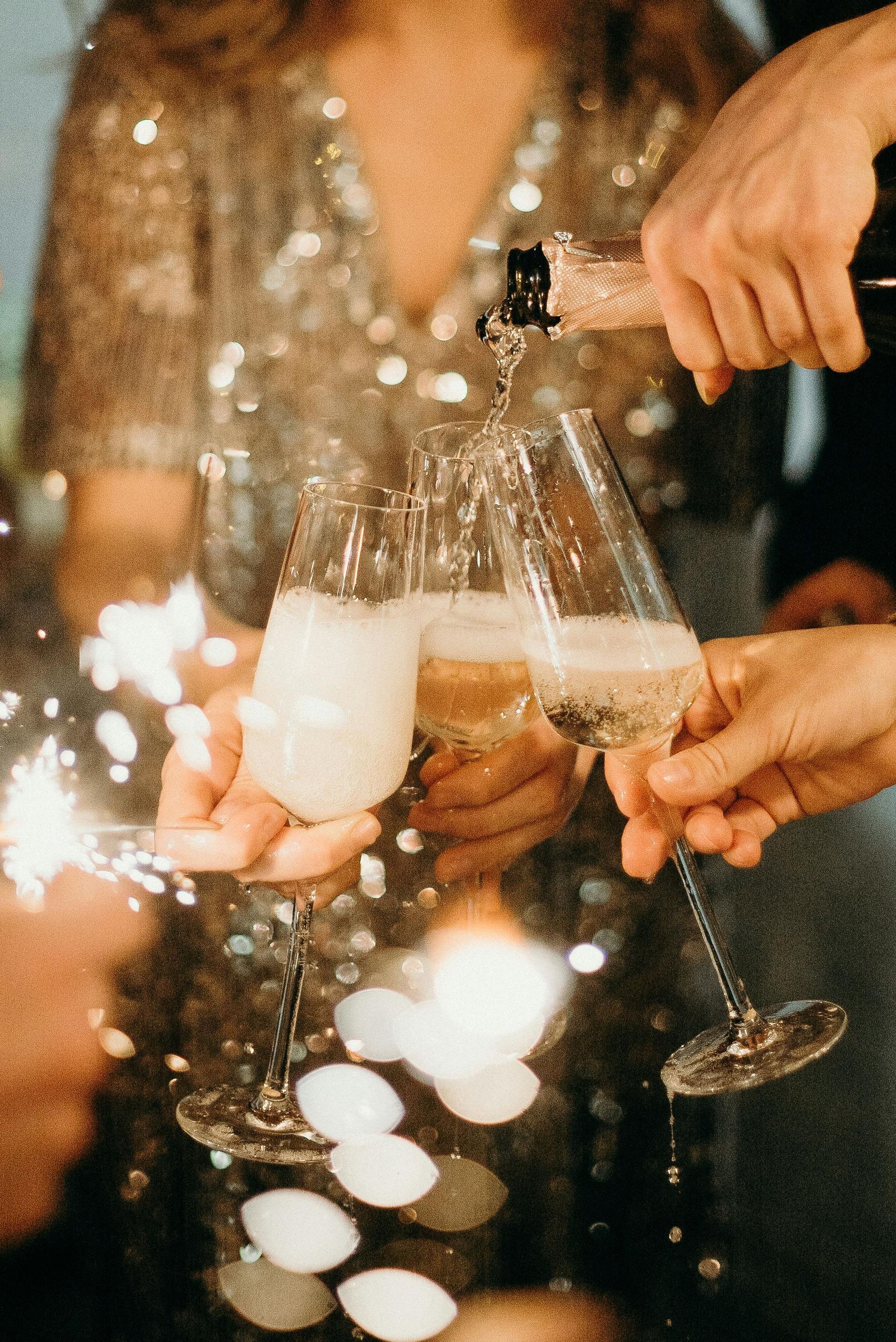 Champagne is poured into three champagne glasses; the celebration continues with sparklers.