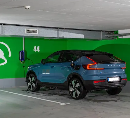 Ein blauer Volvo-Elektrofahrzeug lädt in einem Parkhaus. Grüne Wand mit Ladestation und Stellplatznummer 44.