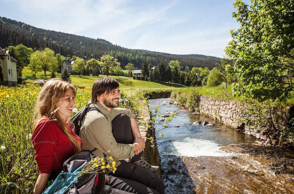 Ein Paar sitzt an einem Bach und genießt die Natur. Grüne Landschaft, sonniger Tag.