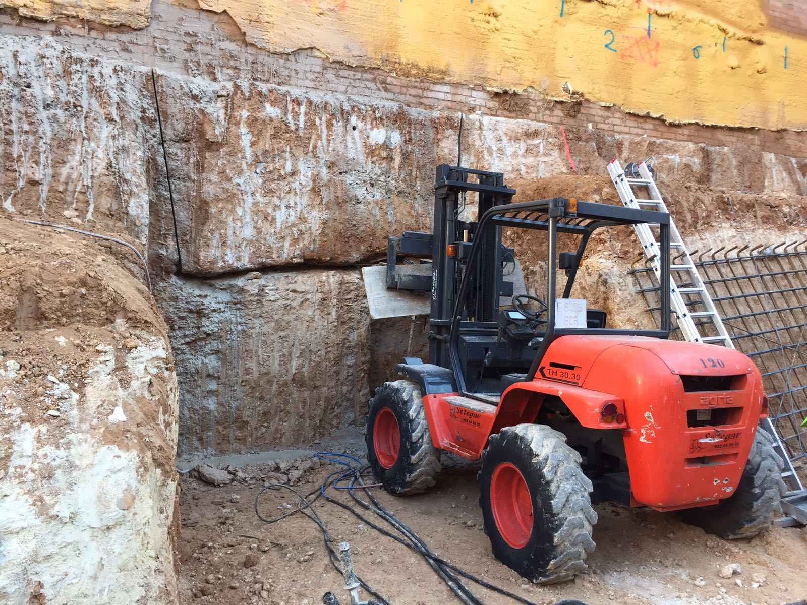 Una carretilla elevadora roja está estacionada frente a una gran pared de roca.