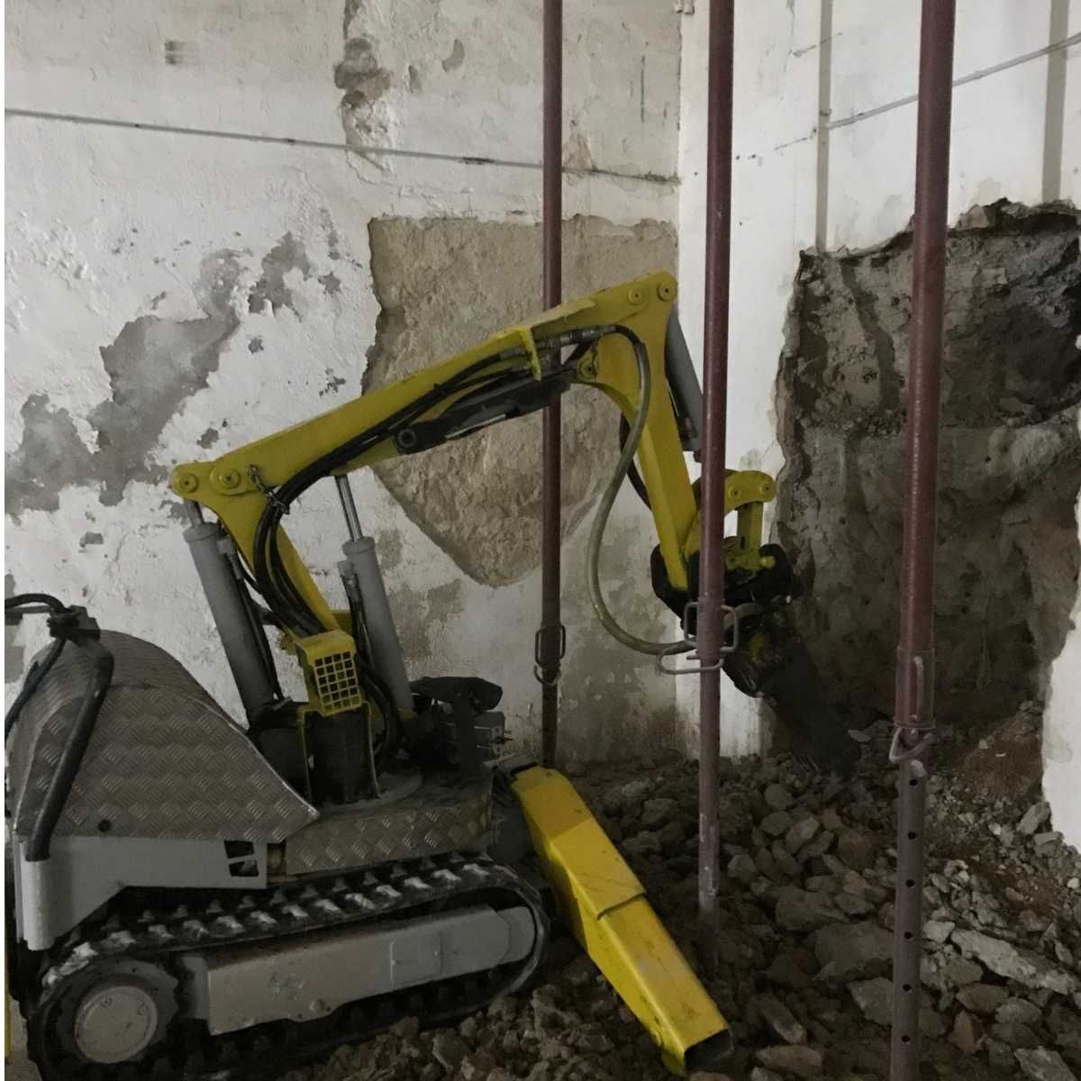 Una excavadora amarilla está parada frente a una pared con un agujero en ella.