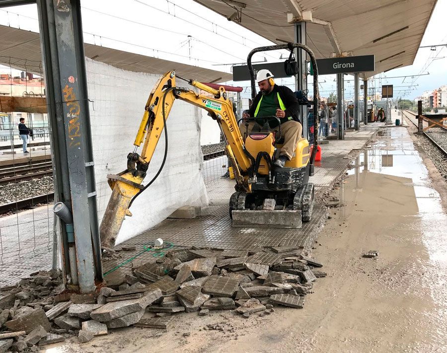 Un hombre conduce una pequeña excavadora en una plataforma de tren.