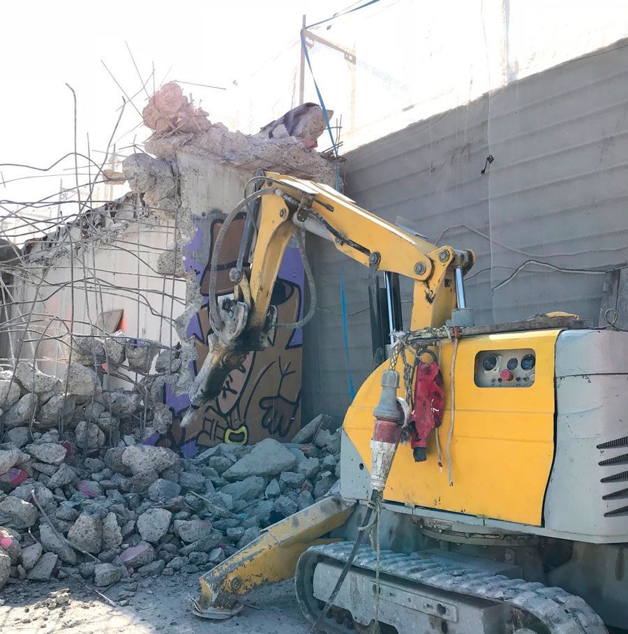 Una excavadora amarilla y blanca está demoliendo un edificio.