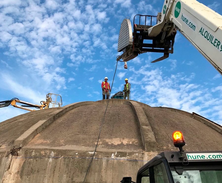 Dos hombres están de pie encima de una gran cúpula con una grúa en el fondo.