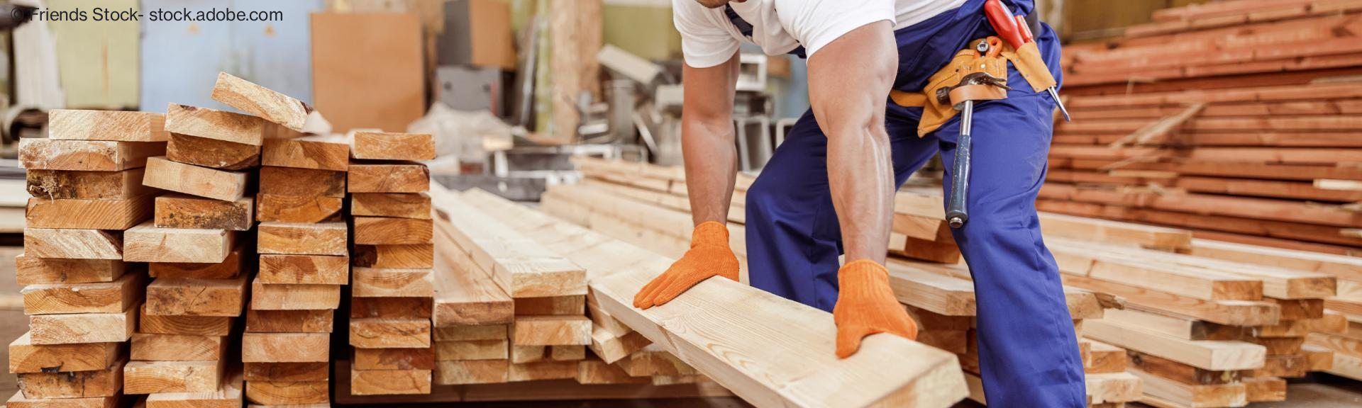Muskulöser Handwerker hebt einen Holzbalken an