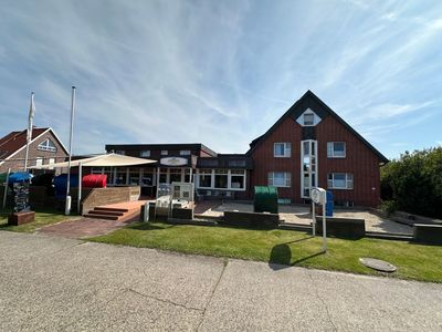 Rotes Backsteingebäude mit mehreren Stockwerken, Balkonen und einem roten Ziegeldach. 