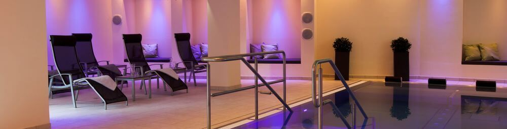 Sandstrand mit hohem Gras im Vordergrund, Meer und untergehende Sonne im Hintergrund.