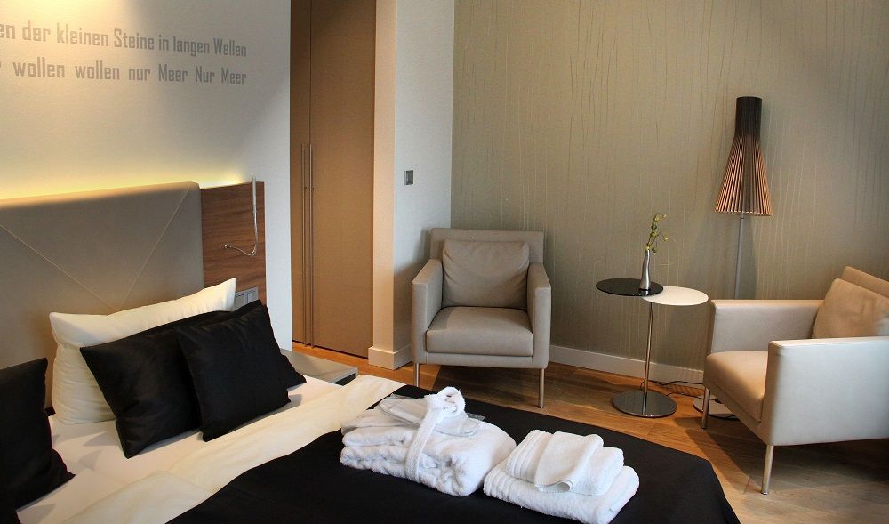 Hotelzimmer mit Bett, Sessel und großem Fenster mit gemusterten Vorhängen.