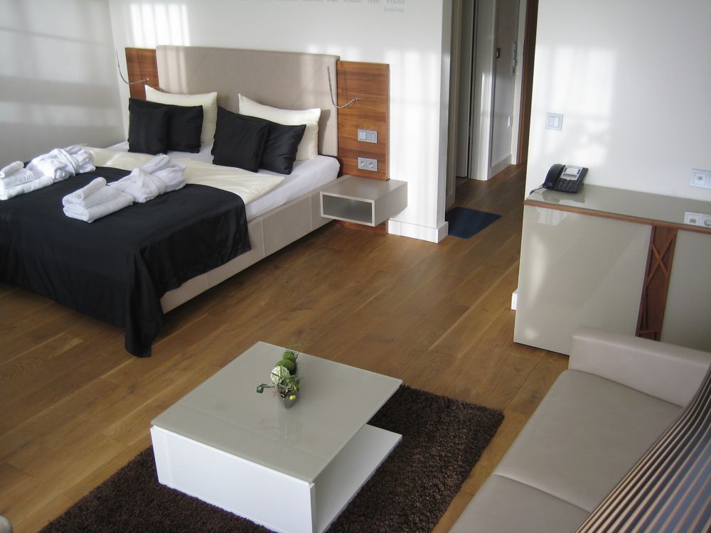Modernes Hotelzimmer mit Bett, Couch und Couchtisch. Holzböden, schwarz-weiße Bettwäsche.