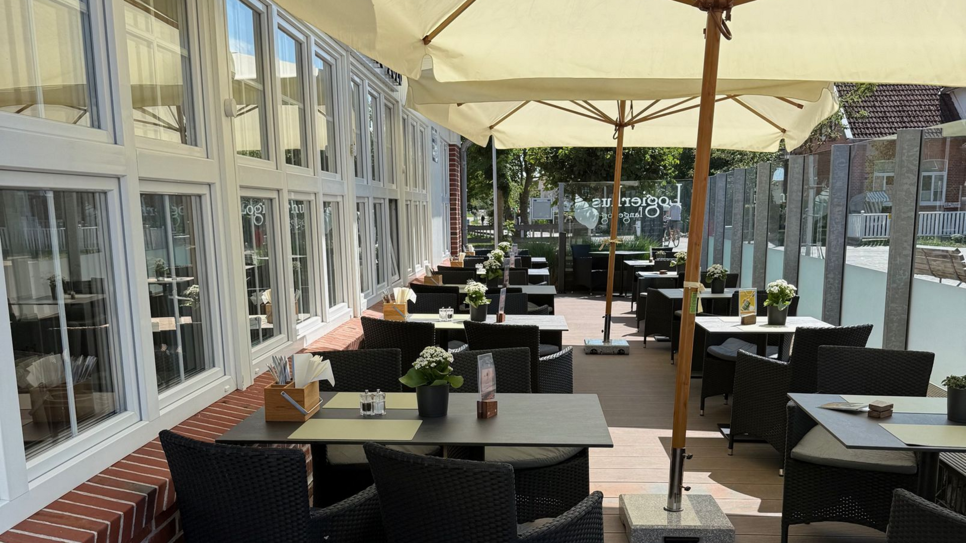 Sitzplätze im Restaurant im Freien unter Sonnenschirmen mit Tischen, Stühlen und Fenstern.