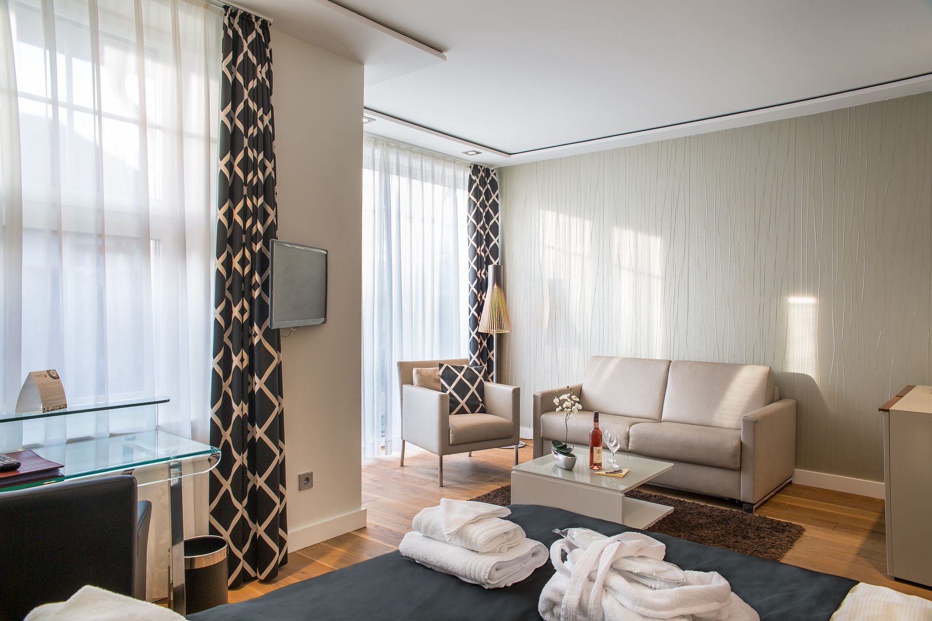 Hotelzimmer mit Bett, Sessel und großem Fenster mit gemusterten Vorhängen.