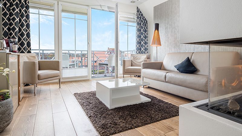 Sandstrand mit hohem Gras im Vordergrund, Meer und untergehende Sonne im Hintergrund.