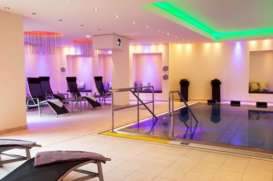 Sandstrand mit hohem Gras im Vordergrund, Meer und untergehende Sonne im Hintergrund.