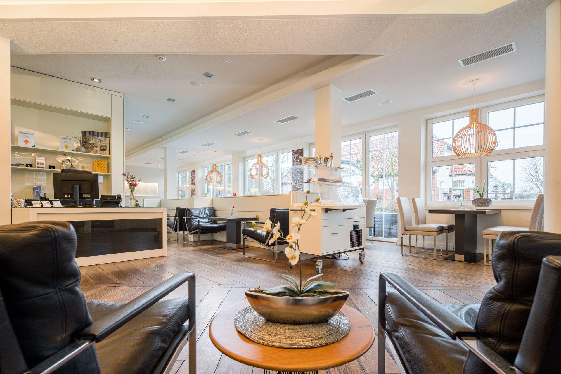 Großzügiger, moderner Wartebereich mit Ledersesseln, Holzboden und großen Fenstern.