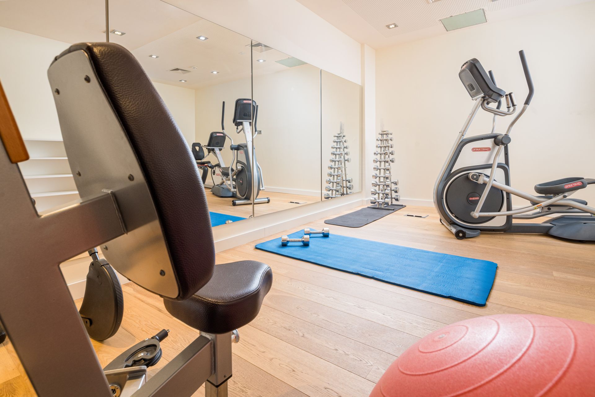 Heim-Fitnessstudio mit Trainingsgeräten, Spiegel und rosa Gymnastikball.