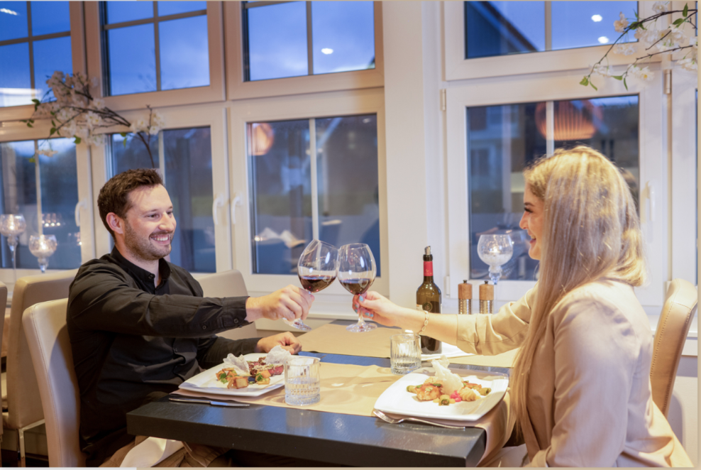 Sandstrand mit hohem Gras im Vordergrund, Meer und untergehende Sonne im Hintergrund.