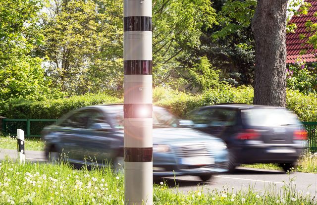 Eine Reihe von Autos fährt neben einem Mast eine Straße entlang.