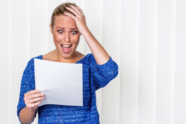 Eine Frau in einem blauen Pullover hält ein Stück Papier in der Hand.