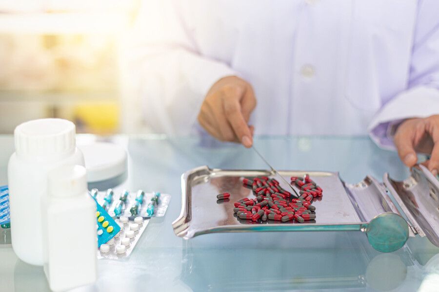 Un operario de laboratorio manipula cápsulas rojas en una bandeja junto a frascos de medicamentos y envases tipo blíster.