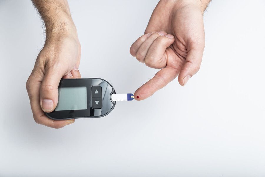 Manos sosteniendo un medidor de glucosa y una tira reactiva con una gota de sangre en la punta.