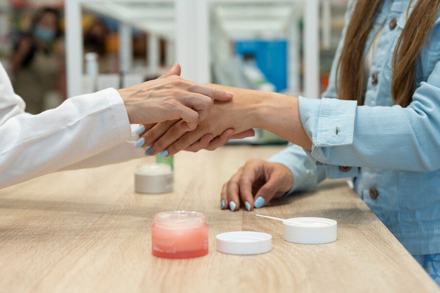 Manos que se encuentran sobre una mesa con frascos de cosméticos en un luminoso entorno de tienda o salón de belleza.