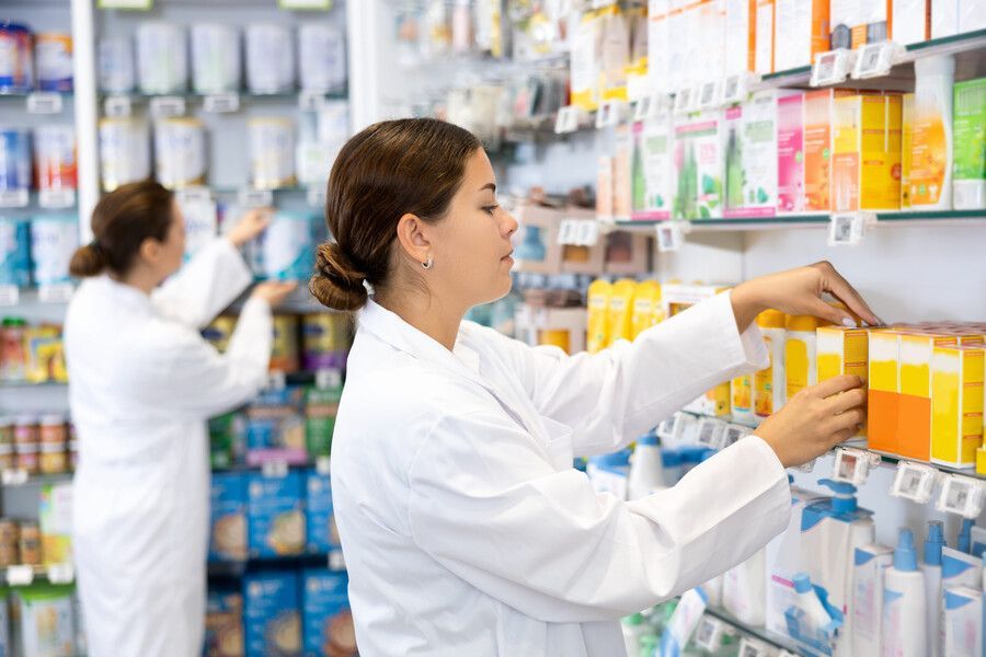 Farmacéuticos reponiendo estantes con cajas de medicamentos en un pasillo de la farmacia.