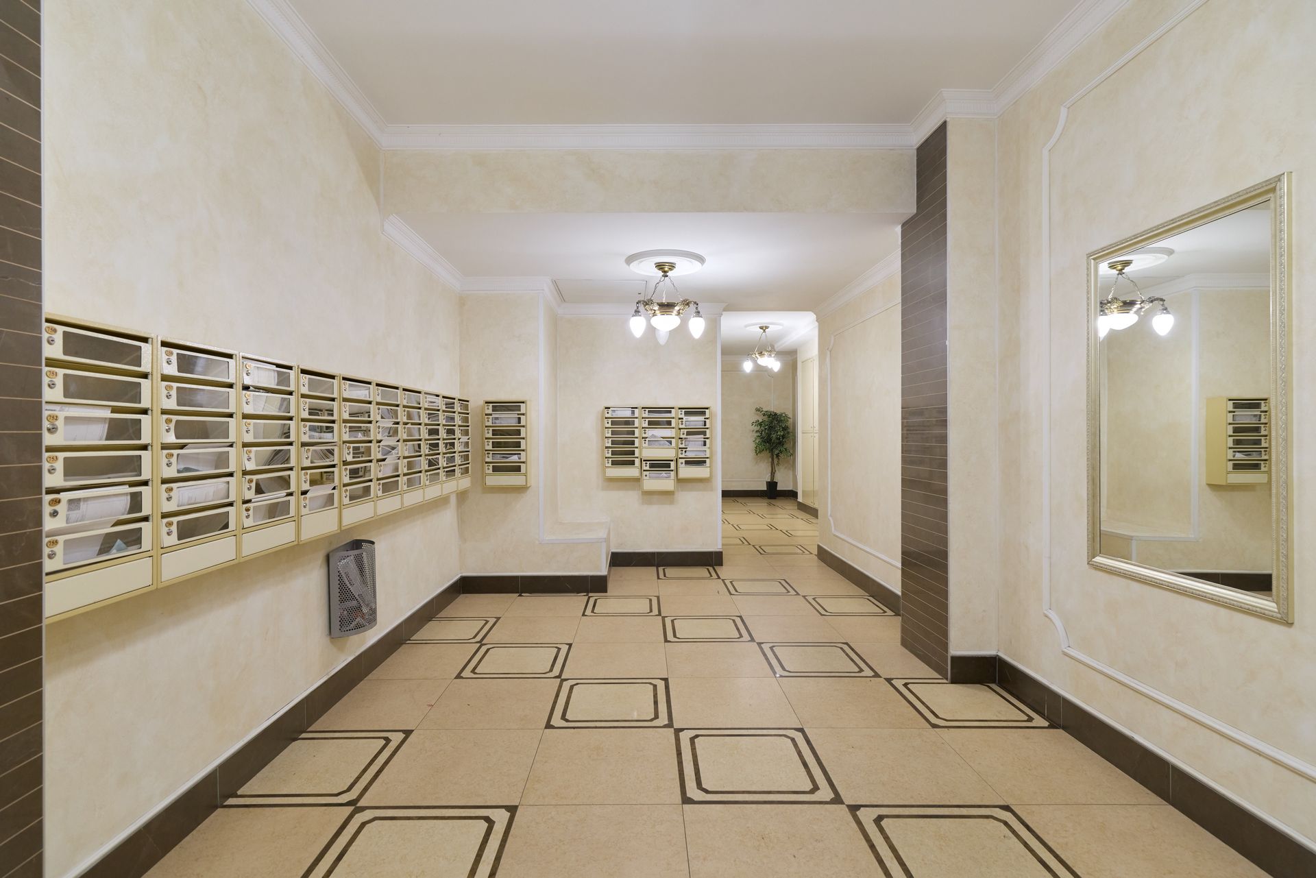 Hall d'immeuble avec boîtes aux lettres à gauche, miroirs à droite et sol beige à motifs noirs.