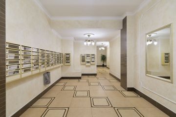 Hall de résidence avec des boîtes aux lettres, des murs blancs, un grand miroir mural et un sol à motifs.